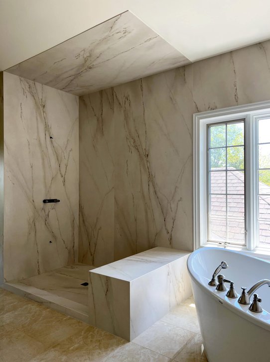 White stone shower walls with gray veins, a stone bench and a soaking tub